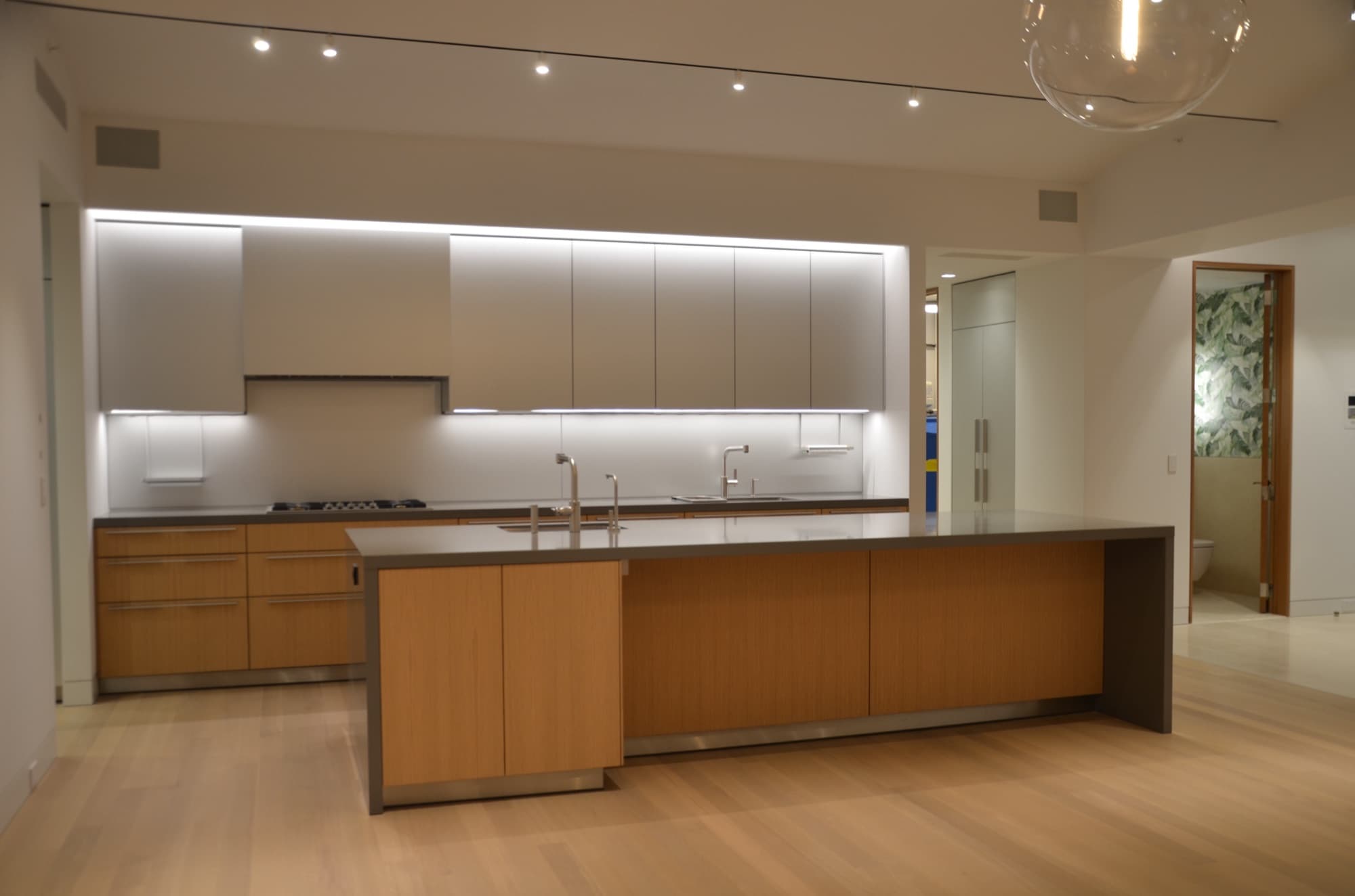 Installed oak and grey-stone kitchen — long island, integrated lighting, light wood floor