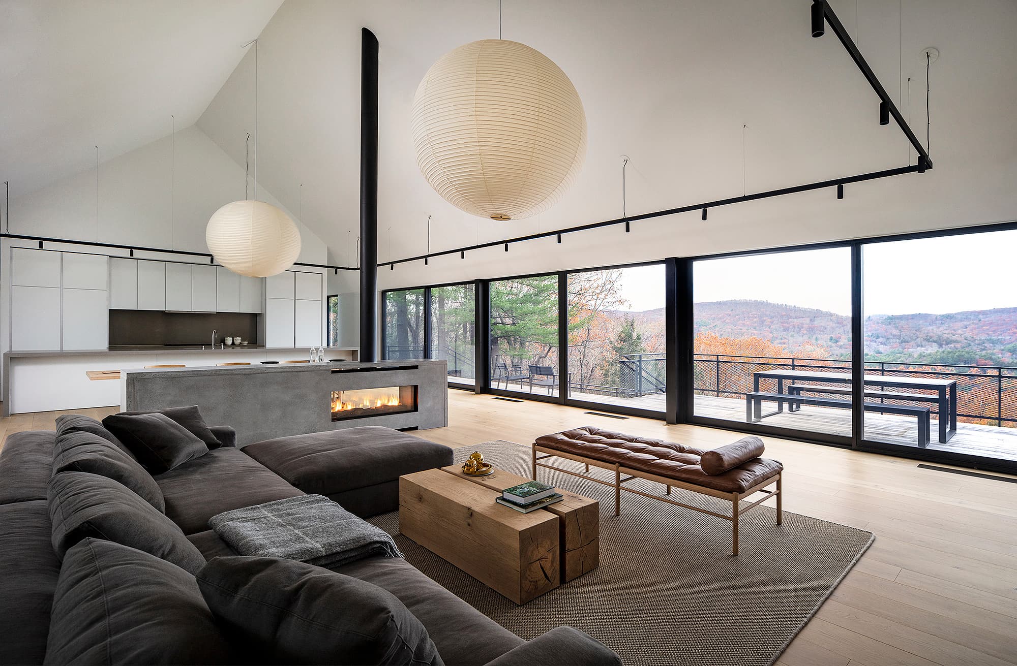 Bulthaup New York residence — open living kitchen with a double-sided concrete fireplace, paper-lantern pendants, and a forest view through full-height glass