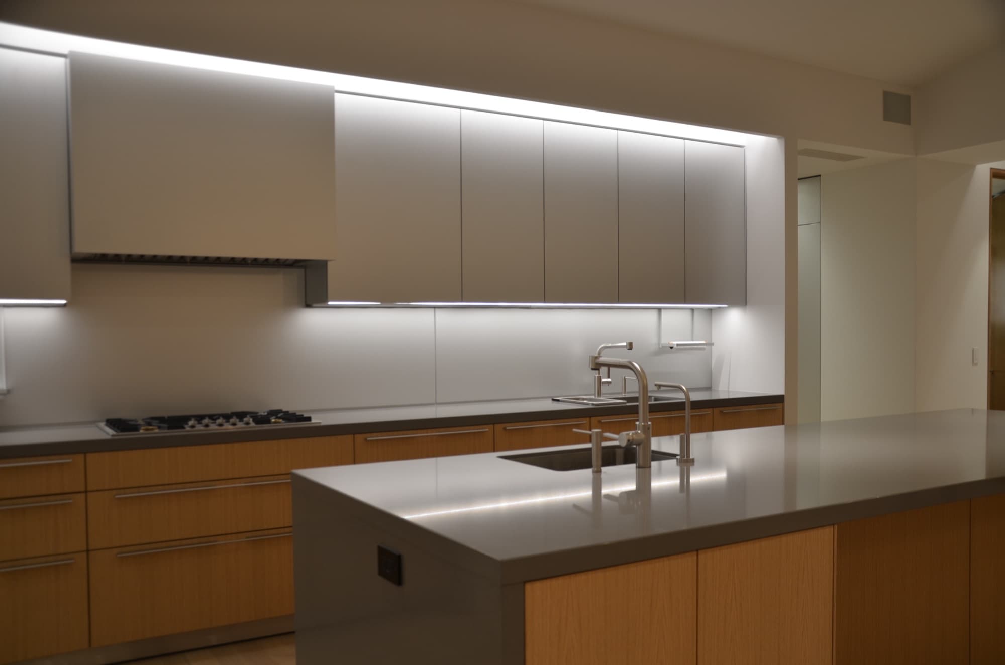 Kitchen in oak and grey stone with white upper cabinets and integrated under-cabinet lighting