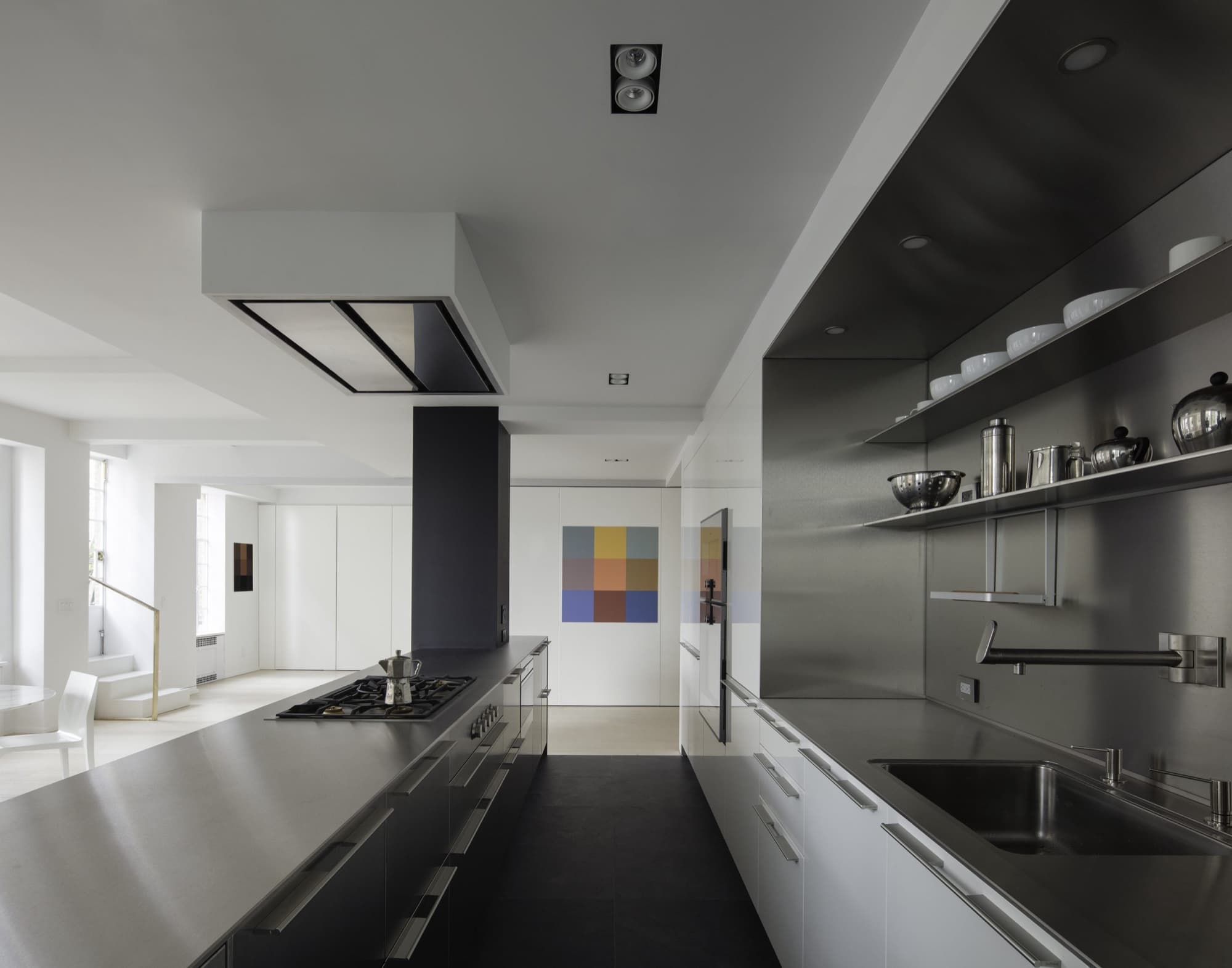 Stainless-steel galley kitchen with open shelving and a colour-grid artwork on a white wall