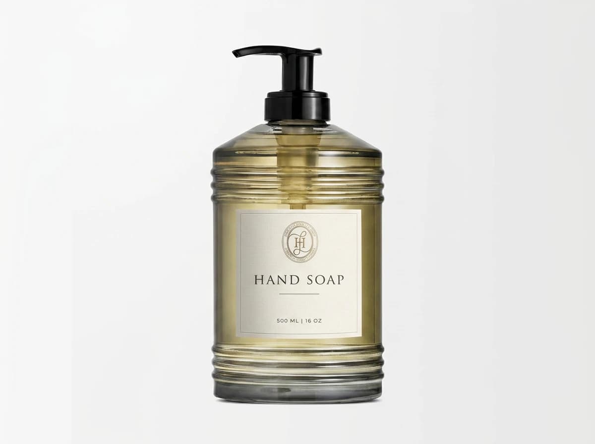 Homelistic hand soap in amber-tinted ribbed glass with a black pump — the seal and HAND SOAP set on a square warm-white label