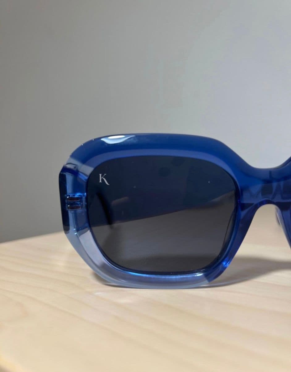 A translucent cobalt-blue KOHL frame on warm wood, the monogram etched into the lens