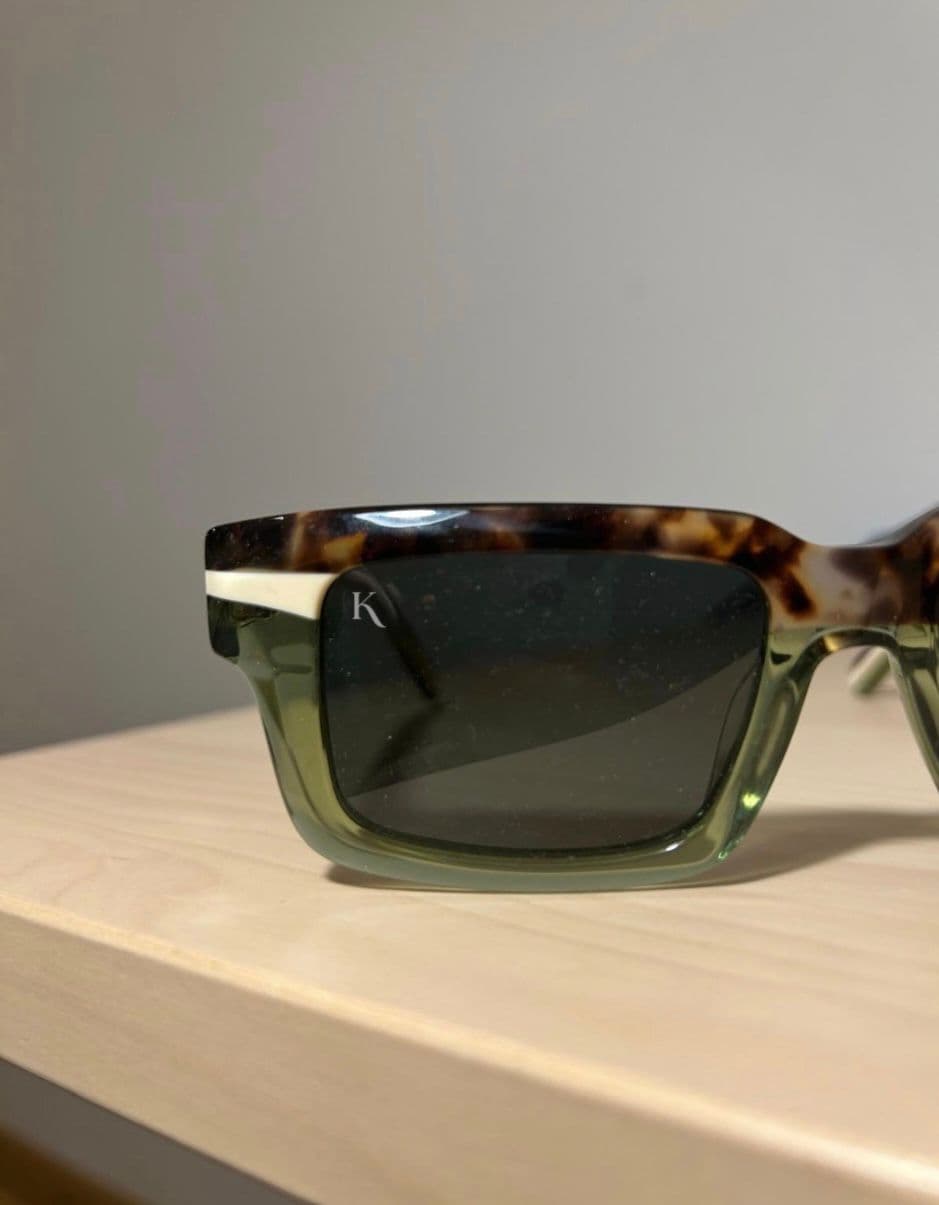 A KOHL frame in translucent olive with a tortoise brow, the monogram etched into the lens