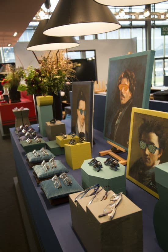A KOHL retail presentation — frames arranged on blue cushions beside classical portraits whose subjects wear the sunglasses
