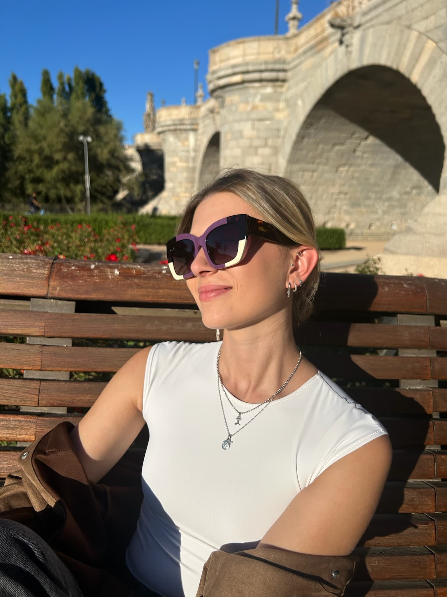 A model in golden light wearing the iris-and-tortoise KOHL frame, the stone arches of a Madrid bridge behind her
