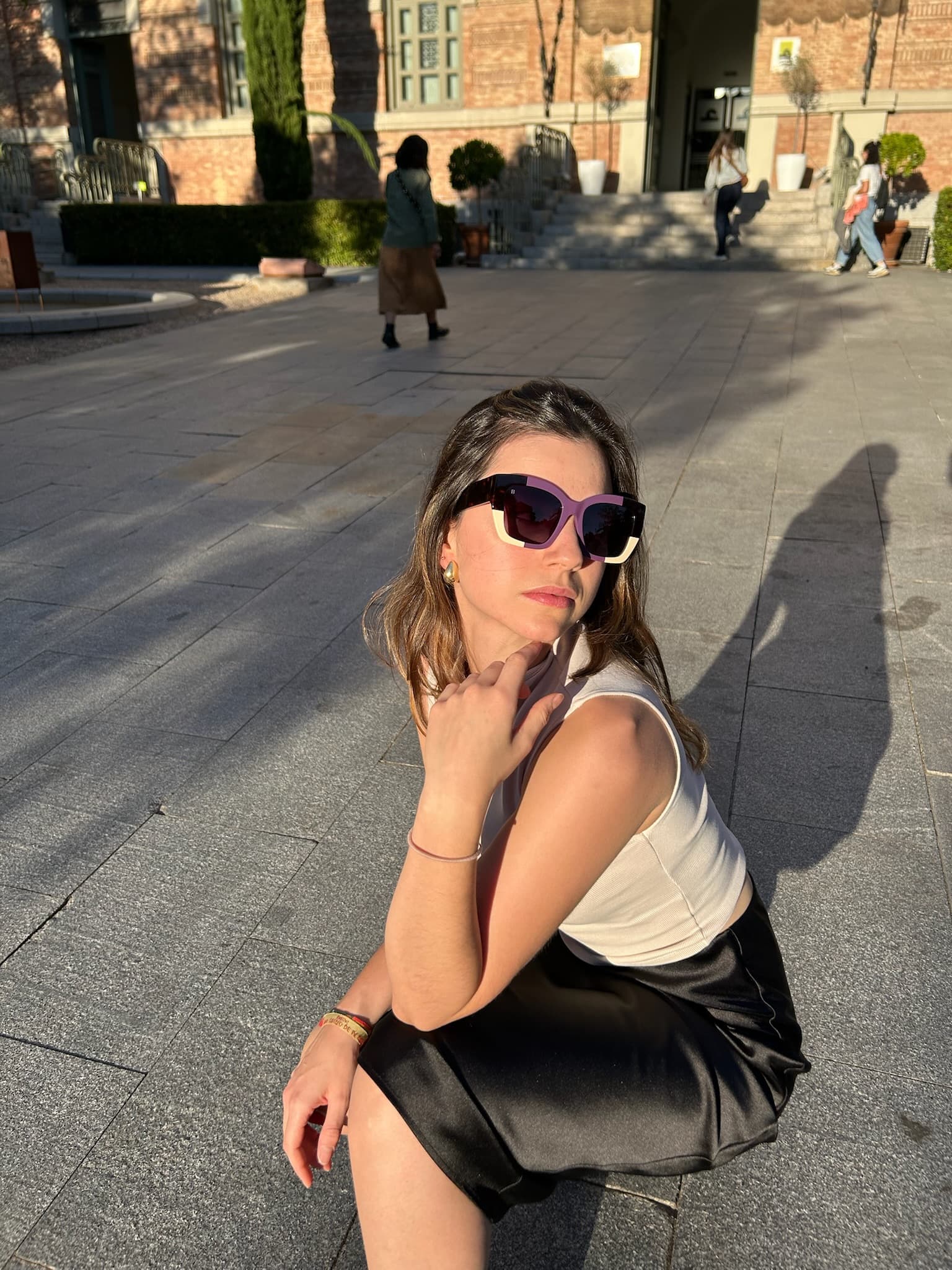 A model in a plaza at golden hour wearing the lilac color-blocked KOHL frame, long shadow behind